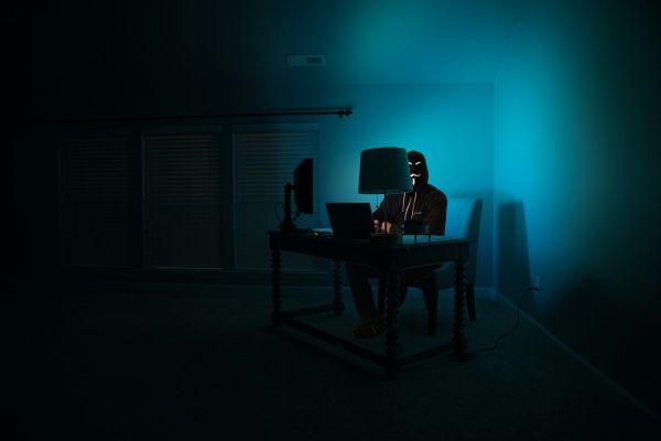 man in zwarte hoodie en een masker op ziet in een donkere kamer achter een computer